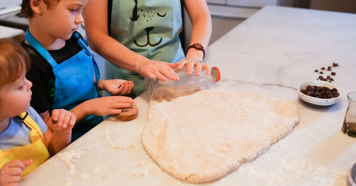 Des enfants et un parent préparant des cookies ensemble dans une cuisine chaleureuse, favorisant le temps de connexion familiale.