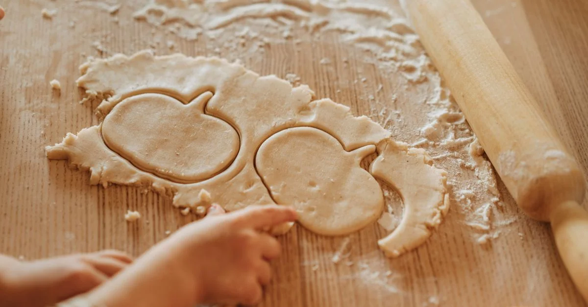 Un enfant fabriquant des biscuits en forme de citrouille avec de la pâte, parfait pour Halloween ou Thanksgiving.