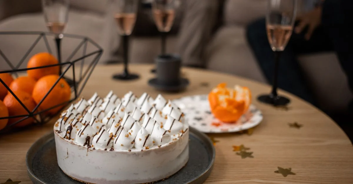 Une mise en scène de dessert élégante avec gâteau, oranges et verres à vin sur une table en bois.