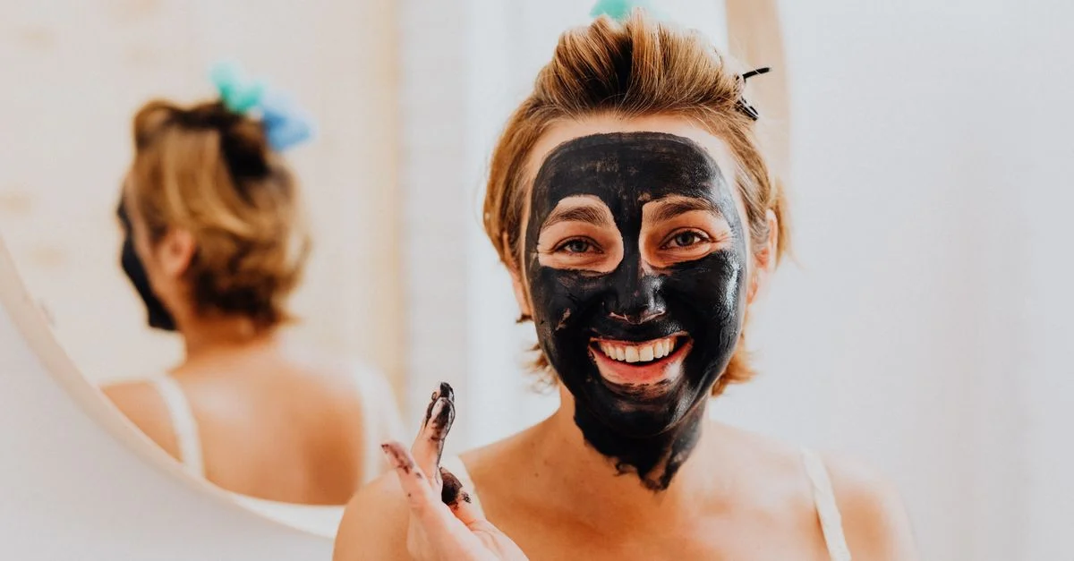 Une femme appréciant sa routine de soin de la peau avec un masque facial noir à l'intérieur.
